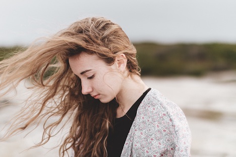 Woman looking downward and letting the wind blow through her hair. 